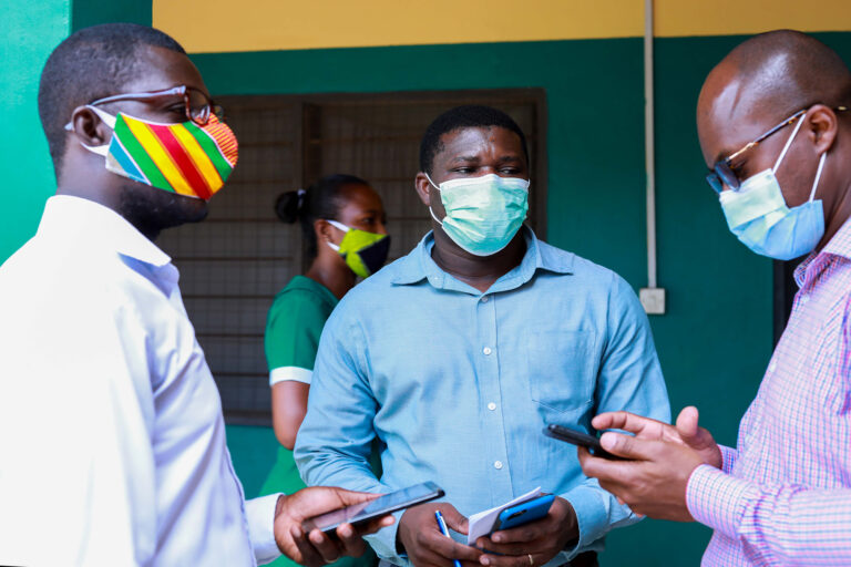 Three men wearing face masks looking at their mobile phones