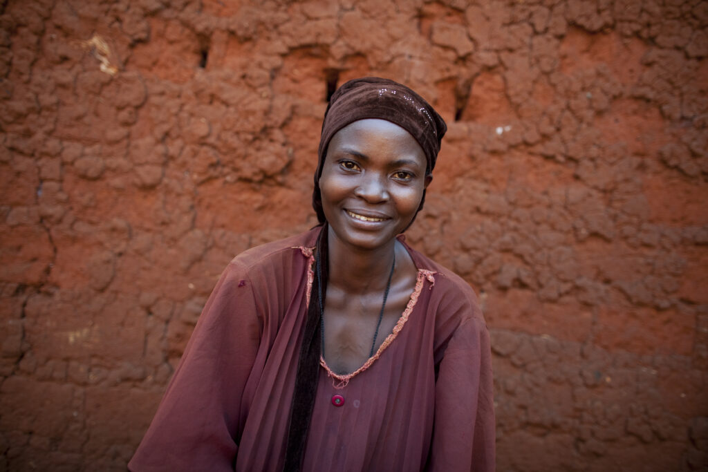 Woman in Benin smiling in front of a burnt orange wall